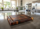 The Beefy BBQ Board® 18" x 15" Cutting Board by BBQ Boards® with metal handles sits on a kitchen island in a modern, bright kitchen featuring white cabinets, stainless steel appliances, and potted plants by the window.