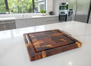 The BBQ Boards® Beefy BBQ Board® 18" x 15" Cutting Board with metal handles rests on a white marble kitchen island, with modern appliances, a sink, and large windows in the background.