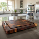 The Beefy BBQ Board® 18" x 15" Cutting Board by BBQ Boards® with metal handles rests on a modern kitchen island, surrounded by white cabinets, stainless steel appliances, and bright natural light from a large window.