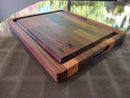 The BBQ Boards® Big BBQ Board® 18 x 15 Reversible Cutting Board, with built-in handles, juice groove, light and dark wood patterns, and a BBQ-themed engraved corner logo, rests on a reflective surface.