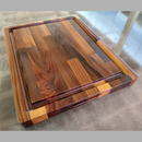 The Big BBQ Board® 18 x 15 Reversible Cutting Board by BBQ Boards® is a medium, rectangular wooden board with brown and tan tones, a groove around the edge, branded logo in one corner, and sits on a reflective surface for added style.