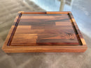 The Big BBQ Board® 18 x 15 reversible cutting board by BBQ Boards® features a juice groove and engraved logo in one corner, shown on a reflective surface.