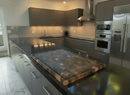 Modern kitchen with dark cabinets, stainless steel appliances, a large island, and the BBQ Boards® Biggest BBQ Board® 36 x 24 Reversible Cutting Board on the counter. White marble floor tiles brighten the clean, well-lit space.
