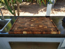 The BBQ Boards® Biggest BBQ Board® 36 x 24 Reversible Cutting Board sits on a dark outdoor countertop by a sink, with trees and plants in the background.