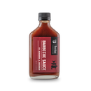 A glass bottle with a black cap holds Bourbon Barrel Foods Barbecue Sauce with Bourbon and Sorghum, featuring a red label with pig and cow illustrations.