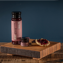 Two jars—one tall, one small—of Bourbon Barrel Foods Black Raspberry Jam sit on a wooden tray beside a biscuit topped with the jam. The background is dark blue and the tray rests on a wooden surface.