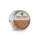 An open round tin of Bourbon Barrel Foods Bourbon Smoked Cinnamon Sugar reveals coarse crystals inside. The label reads "slow. small. simple."—perfect for adding bourbon barrel smoked flavor to desserts and treats.