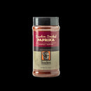 A 4.5 oz (128g) plastic container of Bourbon Barrel Foods Bourbon Smoked Paprika features a red, gold, and tan label with a bourbon barrel illustration, highlighting rich paprika smoked in Louisville, Kentucky.