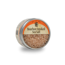 A round metal tin of Bourbon Barrel Foods Bourbon Smoked Sea Salt features a coarse, light brown finishing salt and an orange and cream lid, displayed against a plain white background.