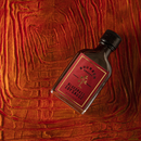 A small bottle of Bourbon Barrel Foods Bourbon Smoked Soy Sauce with a red label and black cap rests at an angle on a textured red and orange surface.
