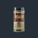 A clear spice jar of Bourbon Barrel Foods Bourbon Smoked Togarashi with a black lid, labeled with red and gold wave patterns plus bourbon barrel and cocktail glass graphics, reflecting its colorful, umami-rich Japanese-inspired seasoning inside.