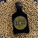 A bottle of Bourbon Barrel Foods Imperial Double Fermented Bluegrass Soy Sauce with a gold label rests on a surface scattered with soybeans.