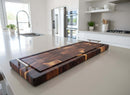 The Burly BBQ Board® 35 x 12 Cutting Board by BBQ Boards® with metal handles rests on a white kitchen island in a bright, modern kitchen accented by stainless steel appliances and minimalist decor.
