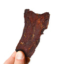 A hand holding a piece of Elijah's Xtreme Pineapple-Mango Habanero Beef Jerky against a plain white background.