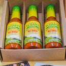 Three bottles of Elijah’s Xtreme Roasted Cayenne and Jalapeño Pepper Sauce are neatly lined up in an open cardboard box on a wooden surface.