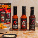Three bottles of Elijah's Xtreme World's Hottest Trio Hot Sauce Variety Pack are on a countertop with their box behind them. Nearby sit bowls of noodles and cheese. The labels—Ghost Pepper, Xtreme Regret, and Carolina Reaper—promise extreme heat.