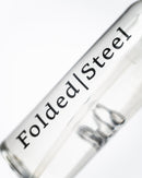 A close-up of Folded Steel Knife Oil in a transparent tube labeled Folded Steel, photographed at an angle on white—perfect for storing or applying oil to high carbon steel blades from the Folded Steel brand.