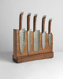 The Folded Steel Magnetic Knife Block by Folded Steel displays five patterned folded steel kitchen knives with wooden handles upright in a matching wooden knife block against a plain light background.