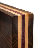 Close-up of a wooden cutting board with decorative dark, light, and reddish-purple wood strips. Its smooth surface pairs perfectly with the Folded Steel Magnetic Knife Block from Folded Steel for stylish knife storage.