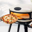 A 16-inch pizza on a peel held in front of a Gozney Arc XL Outdoor Pizza Oven, featuring a digital display showing 950 degrees.