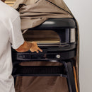 Someone in a white shirt lifts the water-repellent Gozney Dome Gen 2 Series Stand Cover from a black Gozney outdoor pizza oven, revealing its control panel and cooking surface against a crisp white wall.