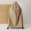 The Gozney Dome Gen 2 Series Stand Cover by Gozney, a water-repellent oven and stand cover, protects a wheeled oven. It stands on a light floor near a wooden slat wall, with the Gozney logo visible.