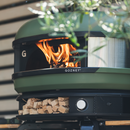 Olive green Gozney Dome Wood outdoor pizza oven with a wood-fired flame inside and a stack of kiln-dried hardwood stored on the shelf below.