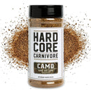 A Hardcore Carnivore BBQ Rub Sampler Set spice jar labeled CAMO Game and Lamb Seasoning sits before a burst of brown seasoning, highlighting bold flavor—ideal for any BBQ seasoning bundle from Hardcore Carnivore.
