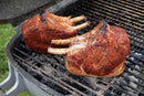 Two large bone-in pork chops grill over charcoal on an outdoor barbecue, showcasing bold sear marks and a smoky char from Hardcore Carnivore Red All Purpose Seasoning by Hardcore Carnivore.