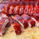 Close-up of juicy, sliced barbecued ribs coated in Hardcore Carnivore Sweet BBQ Rub, featuring a glossy caramelized glaze and sweet seasoning, served on a wooden cutting board.