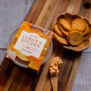 An In The Curious Kitchen Beer Cheese 2 Pack Kentucky Original Spread sits on a wooden board beside a bowl of round toasted bread slices, with creamy cheddar spread on a wooden knife ready to sample.