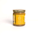 A glass jar of In The Curious Kitchen Bourbon Honey Mustard, handcrafted in Kentucky, with a gold lid and a bright yellow floral label reading "Stay Awhile Won’t You?"—perfect for charcuterie boards, displayed on a white background.
