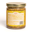 A glass jar with a gold lid in the In The Curious Kitchen Bourbon-Infused Gourmet Gift Set holds stone-ground mustard. Its label lists nutrition facts, a barcode, and ingredients such as mustard seed, vinegar, honey, water, and Kentucky bourbon.