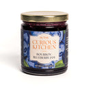 A glass jar of In The Curious Kitchen Bourbon-Infused Gourmet Gift Set jam with a gold lid. The label features blueberries, displays 9 oz (255g), and highlights Kentucky bourbon—ideal for any gourmet gift set.
