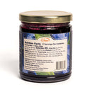 A glass jar from In The Curious Kitchen Bourbon-Infused Gourmet Gift Set, featuring blueberry preserves with 17 servings. The label highlights ingredients like blueberries, lemon juice, sugar, and vanilla extract.