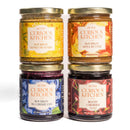 The In The Curious Kitchen Bourbon-Infused Gourmet Gift Set features four jars—Bourbon Honey Mustard, Bourbon Apple Butter, Bourbon Blueberry Jam, and Boozy Cherries—all with colorful, illustrated labels and a hint of Kentucky bourbon.