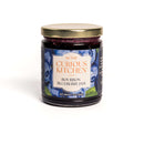 A glass jar with a gold lid labeled In The Curious Kitchen Brunch & Breakfast Jam Trio sits on a white background, featuring images of blueberries and text indicating a net weight of 9 ounces (255g).
