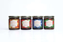 The In The Curious Kitchen Entertaining Jam & Jelly Gift Set features four colorful jars—apple butter, strawberry jalapeño jam, blueberry jam, and hot pepper jelly—perfect for charcuterie boards and styled on a white background.