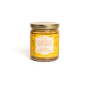 A glass jar of In The Curious Kitchen Southern Gourmet Spread Gift Set, with a gold lid and yellow label, is shown against a white background—perfect for charcuterie boards or gifting from the In The Curious Kitchen brand.