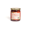 A glass jar with a gold lid containing a red preserve from In The Curious Kitchen, featured in the Southern Gourmet Spread Gift Set. The white label with red borders displays nutrition facts, ingredients, and product info.