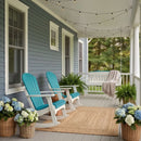 A cozy front porch with two Kanyon Living Adirondack Rocking Chairs in Aruba Blue & White, a white swing draped with a blanket, string lights above, potted hydrangeas and green ferns on a gray wooden floor with a woven rug.