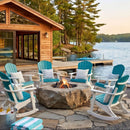 Six Kanyon Living Adirondack Rocking Chairs in Aruba Blue & White are arranged around a stone fire pit on a lakeside patio, with cozy pillows and drinks, a wooden cabin nearby, trees, and a dock overlooking calm water.