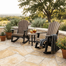 Two Kanyon Living Adirondack Rocking Chair Deluxe Antique Mahogany & Black sit on a stone patio with a small table set for iced tea. A blue blanket is draped over one chair, surrounded by potted plants—an inviting spot from Kanyon Living to relax outdoors.