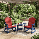 Two Kanyon Living Adirondack Rocking Chairs in red and blue sit under a wooden pergola on a stone patio, separated by a small blue table with a drink and potted plant. Lush greenery and string lights make the setting cozy.