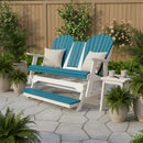 The Kanyon Living Poly Lumber 5′ Adirondack Glider Tall Version in Aruba Blue & White, accented with two cream pillows, adds comfort and style to a stone patio with green potted plants and a small side table.