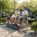 A smiling couple relaxes on the Kanyon Living Poly Lumber 5′ Adirondack Glider Tall Version in blue and light grey, enjoying coffee and cookies in a sunny garden surrounded by hydrangeas and potted plants.