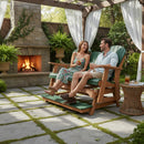 A smiling couple relaxes on the Kanyon Living Poly Lumber 5′ Adirondack Glider Tall Version in Dark Green and Cedar Wood, beneath a pergola in a garden, with an outdoor fireplace glowing behind them among potted plants and white curtains.