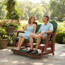 A smiling couple relaxes together on the Kanyon Living Poly Lumber 5′ Adirondack Glider (Tall Version, Dark Green & Cherry Wood), surrounded by colorful flowers and greenery in a sunlit garden.