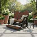 The Kanyon Living Poly Lumber 5′ Adirondack Glider Tall Version Deluxe in Antique Mahogany and Black offers relaxing outdoor seating on your patio, paired with greenery and a table for drinks—perfect for sunny days.
