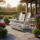 A Kanyon Living Poly Lumber 5′ Adirondack Glider Tall Version Deluxe in Driftwood Grey and White sits on a sunlit patio with potted flowers, a side table holding a coffee cup, and more Kanyon Living outdoor furniture visible in the garden background.
